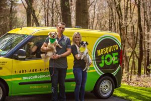 Jessica and Myles owners of Mosquito Joe of Bel Air MD with their dogs Remy and Zoe in front of a Mosquito Joe van.